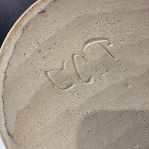 Op de afbeelding: Close-up van de onderkant van een keramische vaas met de letters "EC" gestempeld in de bodem.