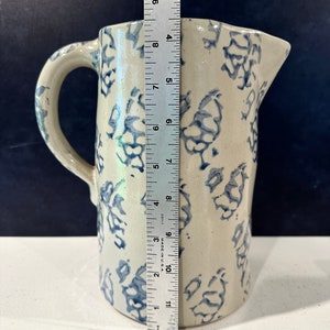 Op de afbeelding: Een witte keramische kan met een blauw-wit bloemenpatroon. De kan heeft een handvat en is ongeveer 30 cm hoog.