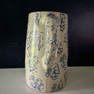Op de afbeelding: Een witte keramische kan met een blauw bloemenpatroon. De kan heeft een handvat en een brede opening.