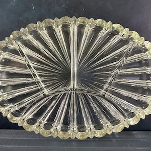 May include: A clear glass serving dish with three sections. The dish has a scalloped edge and a sunburst pattern.