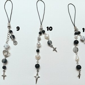 May include: Three black and white phone charms with different designs. The charms feature a dice, a heart, a cross, a spiral, and a star. The charms are attached to black cords.