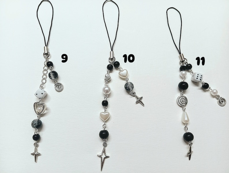 May include: Three black and white phone charms with different designs. The charms feature a dice, a heart, a cross, a spiral, and a star. The charms are attached to black cords.