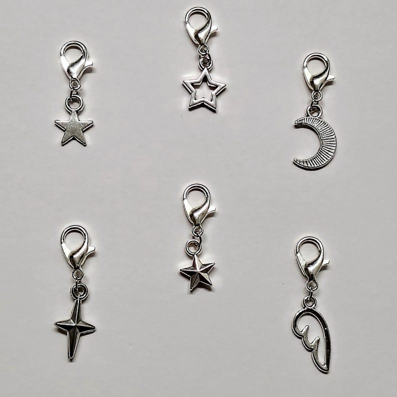 May include: Six silver charm clips with different designs: a star, a crescent moon, a star with a point, a star, a wing, and a star with a point.
