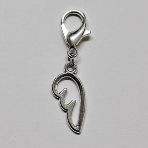 May include: Silver charm with a wing design. The charm has a lobster clasp for attaching to a bracelet or necklace.