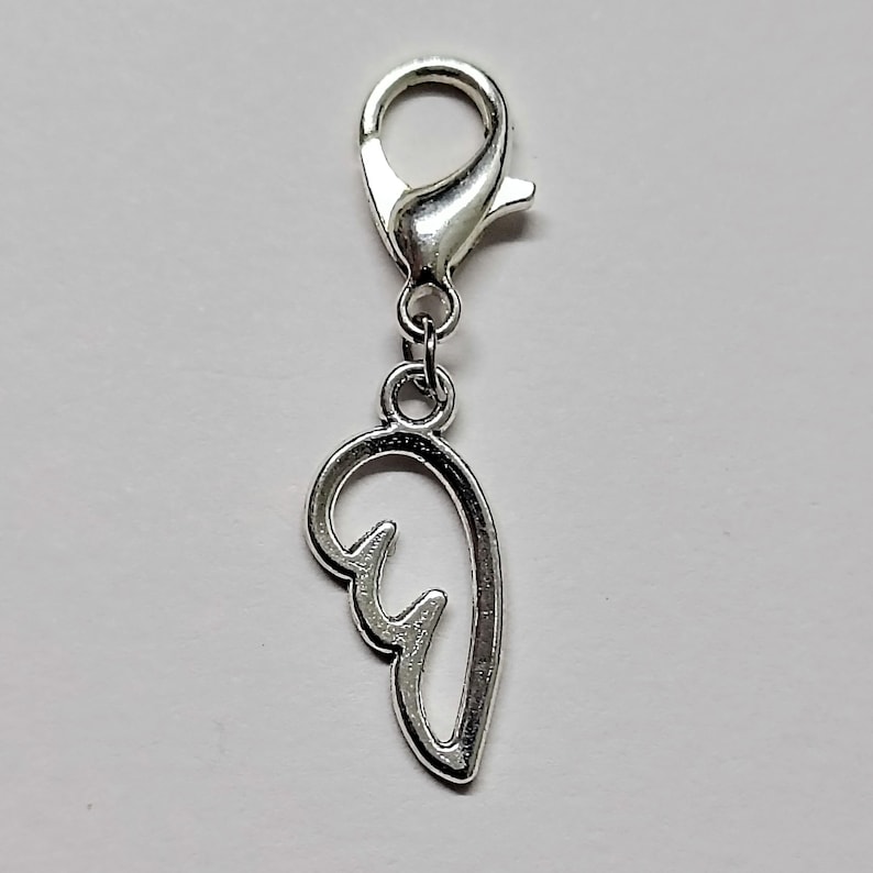 May include: Silver charm with a wing design. The charm has a lobster clasp for attaching to a bracelet or necklace.