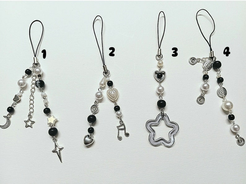 May include: Four black and white phone charms with different designs. The charms feature a crescent moon, stars, a heart, a music note, a star, and a swirl design.