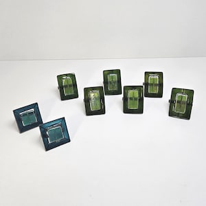 May include: An assortment of rectangular rings with a dark green and teal color scheme. The rings have a square shape with a rectangular inset. The rings are arranged on a white surface.