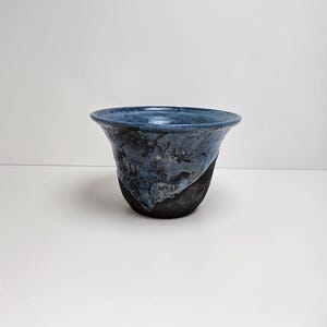 May include: A handcrafted ceramic vase with a flared rim. The vase features a dark blue glaze on the top and a black base, with textured details. The design is a unique, artistic piece, suitable for home decor.