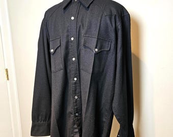 May include: A black long-sleeve shirt with two chest pockets and silver snap closures. A black and white bandana is draped around the collar. The shirt is displayed on a mannequin.