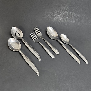 May include: A collection of vintage silverware, including spoons and forks, arranged on a dark gray surface. The silverware has a shiny, silver finish with a decorative floral pattern on the handles. One spoon has a slotted design.