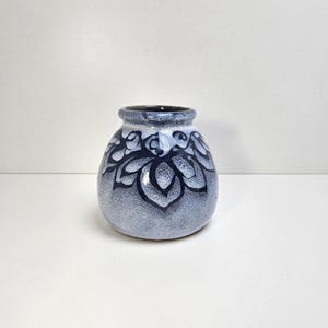 May include: A small, round ceramic vase with a dark blue rim and a light blue body. The vase is decorated with a dark blue floral pattern. The vase is approximately 5 inches tall.