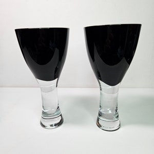 May include: Two black and clear glass wine glasses with a wide bowl and a tall, slender stem.