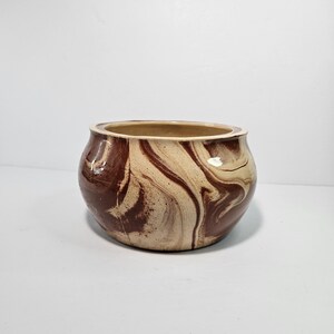 May include: A brown and cream ceramic planter with a marbled design. The planter has a rounded shape and a wide opening.
