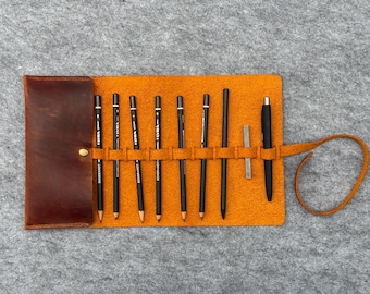 May include: A brown leather pencil roll with a yellow felt interior. The roll has 10 slots for pencils and a separate slot for a pen. The roll is rolled up and tied with a brown leather strap.