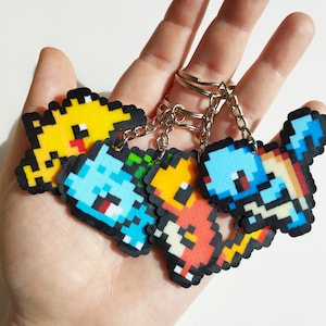 May include: Four pixel art keychains featuring different Pokemon characters. The keychains are made of colorful beads and attached to silver key rings. The characters include a yellow Pikachu, a blue Squirtle, a red Charmander, and a green Bulbasaur.