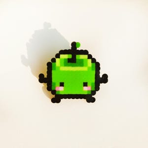 Puede incluir: Personaje de pixel art verde con una pequeña antena en la parte superior de su cabeza. El personaje tiene una cara simple y amigable con ojos negros y mejillas rosadas.