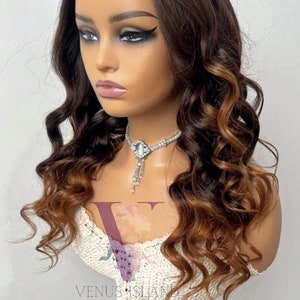 May include: A long, wavy, brown and blonde ombre human hair wig with a lace front. The wig is styled in loose curls and is worn on a mannequin head.