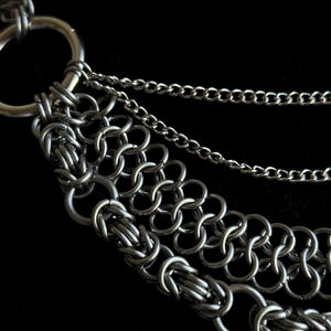 May include: A silver chain necklace with multiple layers of chain links. The necklace has a large, round, silver clasp.