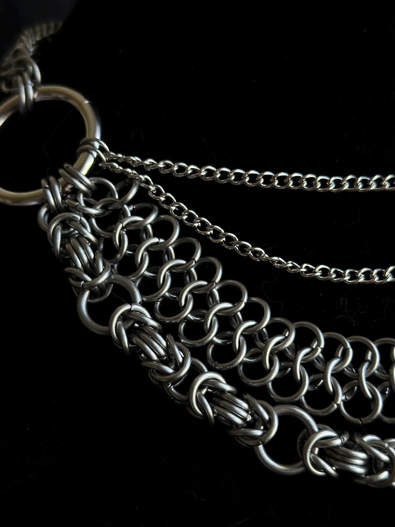 May include: A silver chain necklace with multiple layers of chain links. The necklace has a large, round, silver clasp.