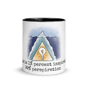 May include: White ceramic mug with a black rim. The mug features a blue and yellow illustration of an iceberg with a lightbulb inside. The text on the mug reads "Genius is 1% inspiration 99% perspiration."