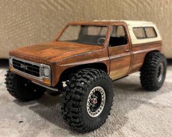 Peut inclure: Modèle réduit de camion GMC marron et blanc avec de gros pneus noirs. Le camion a un aspect vieilli, avec des textures de type rouille sur la carrosserie. Les pneus ont un motif de bande de roulement détaillé et les roues ont des jantes argentées.