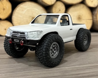 Op de afbeelding: Witte speelgoedtruck met zwarte banden en een zwarte grille. De truck staat op een houten oppervlak.