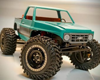 May include: Teal blue pickup truck with black wheels and tires. The truck has a black and silver grill with a Chevrolet logo.