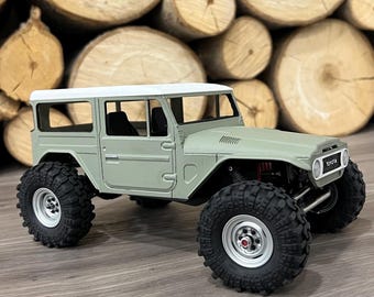 Op de afbeelding: Een groene en witte speelgoedtruck met zwarte banden en een wit dak. De truck staat op een houten oppervlak. De truck heeft het woord "TOYOTA" aan de zijkant.