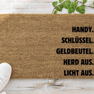 Könnte beinhalten: Eine braune Fußmatte mit dem Text "HANDY. SCHLÜSSEL. GELDBEUTEL. HERD AUS. LICHT AUS."