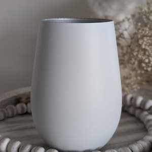 May include: A light gray ceramic vase with a rounded bottom and a wide opening. The vase is sitting on a wooden surface with a string of white beads.