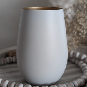 May include: A white ceramic candle holder with a gold rim. The holder is sitting on a wooden surface with white beads.