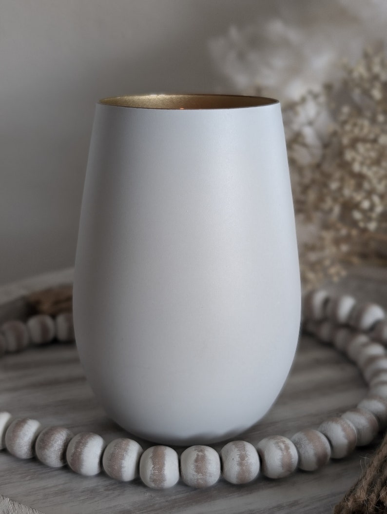 May include: A white ceramic candle holder with a gold rim. The holder is sitting on a wooden surface with white beads.