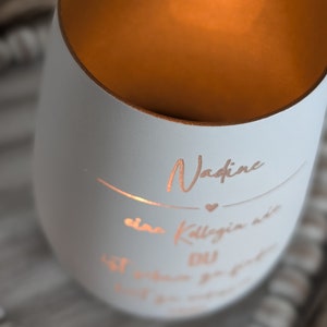 May include: A white candle with a gold rim and a personalized message that reads "Nadine, a colleague we will never forget".
