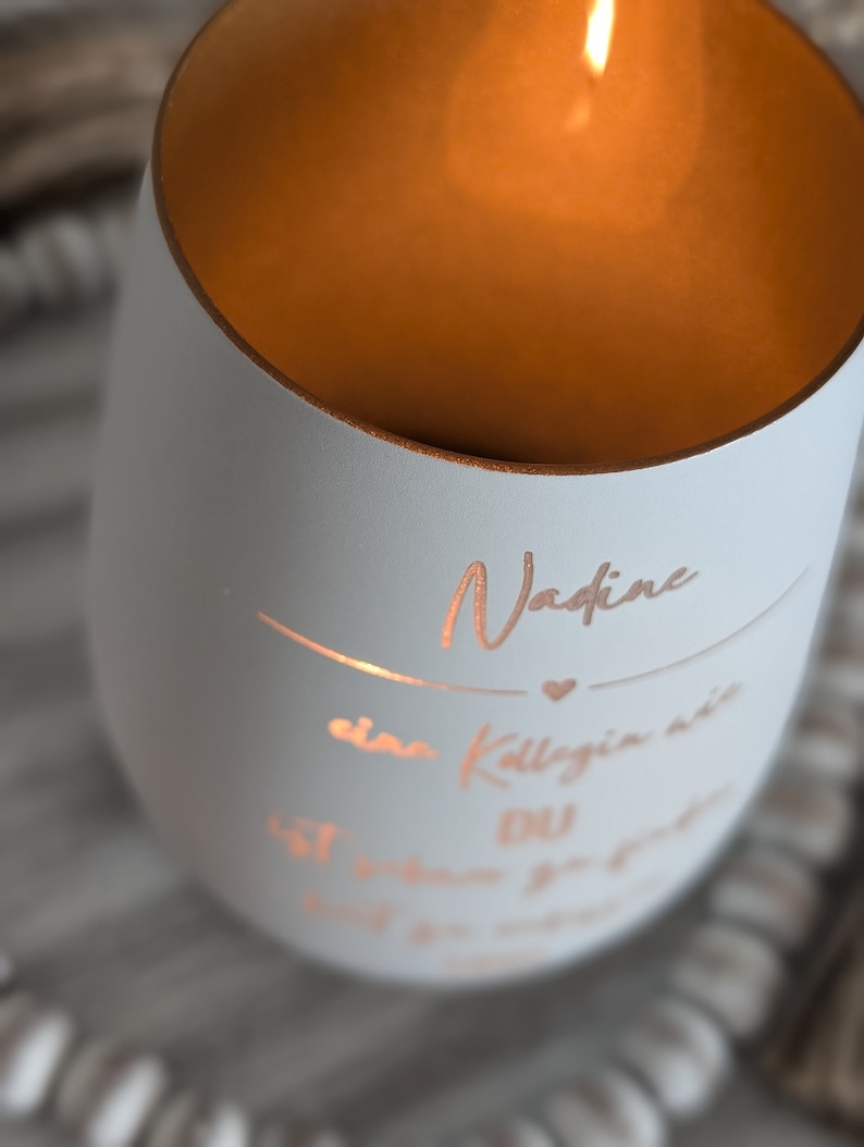 May include: A white candle with a gold rim and a personalized message that reads "Nadine, a colleague we will never forget".
