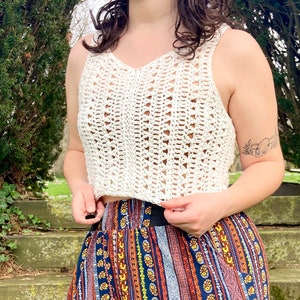 Könnte beinhalten: Ein weißes Häkel-Crop-Top mit einem zarten Lochmuster. Das Top wird mit einem bunten gemusterten Rock getragen.