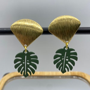 Clip on earrings that have a green powder coated monstera leaf hanging from raw brass charms.