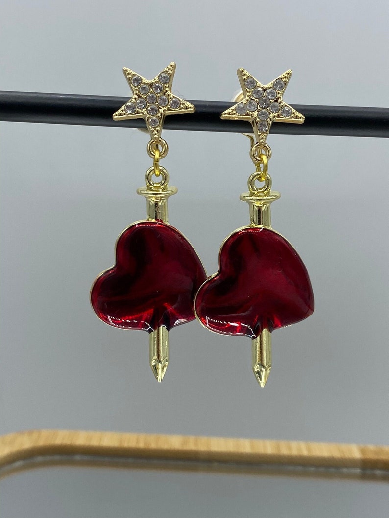 Dangly clip on earrings with red hearts that are pierced by swords, hanging from sparkly stars.