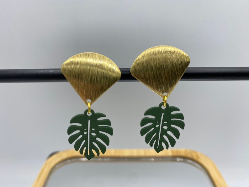 Clip on earrings that have a green powder coated monstera leaf hanging from raw brass charms.