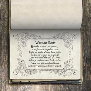 May include: An open book displaying the Wiccan Rede poem. The text is in black, surrounded by an ornate border. The book's pages are off-white, and the cover is a dark color.
