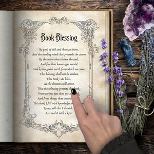 May include: An open book with the title "Book Blessing" in elegant script. The text is surrounded by an ornate border. A hand with a black painted nail points to the text. Lavender and crystals are arranged on a wooden surface.
