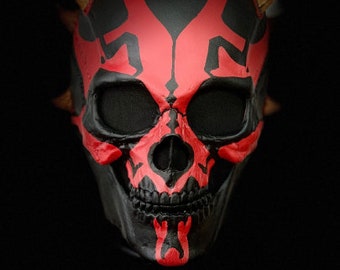 Op de afbeelding: Een rood en zwart schedelmasker met hoorns. De schedel heeft een gedetailleerd ontwerp en is geschilderd in een dreigende stijl.