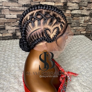 May include: A black braided wig with a lace front and intricate designs. The wig is styled in a high bun with braids extending from the crown. The wig is on a mannequin head with a red and black plaid shirt.