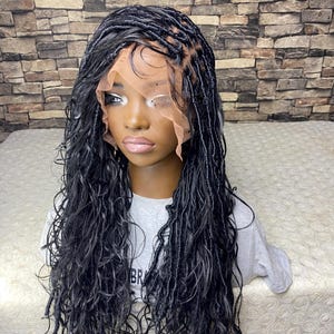 May include: A black wig with long, wavy dreadlocks. The wig features a lace front and is styled on a mannequin head. The mannequin is wearing a gray t-shirt. The background is a brick wall.