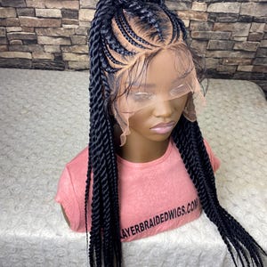Peut inclure: Perruque tressée noire avec un devant en dentelle, présentée sur une tête de mannequin. La perruque combine des tresses en épi de blé et de longues tresses torsadées. Le mannequin porte un t-shirt rose avec le texte LAYERBRAIDEDWIGS.COM.
