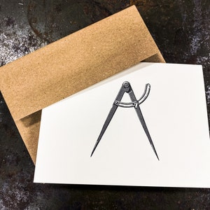May include: A black and white illustration of a compass on a white card with a brown envelope behind it.
