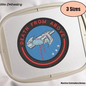 Pode incluir: Design de bordado de máquina de uma nave espacial com o texto "Death From Above" em um círculo com fundo azul e contornos vermelhos e pretos.
