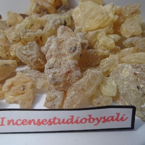 May include: A pile of light amber-colored resin chunks with a slightly frosted appearance. The image includes a small rectangular sign with the text "Incensestudiobysali".