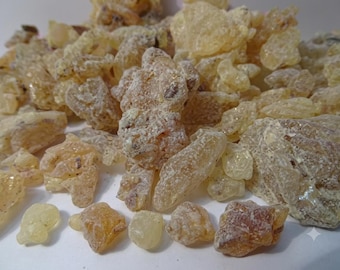 Può includere: Una collezione di piccoli pezzi di resina irregolari e traslucidi in tonalità giallo pallido, ambra e oro chiaro. I pezzi hanno una consistenza cristallina e frastagliata con una polvere bianca opaca e inclusioni marrone scuro.