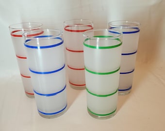 May include: Set of five frosted glass tumblers with colored stripes. The tumblers are clear glass with a frosted finish and have red, blue, and green stripes around the middle.