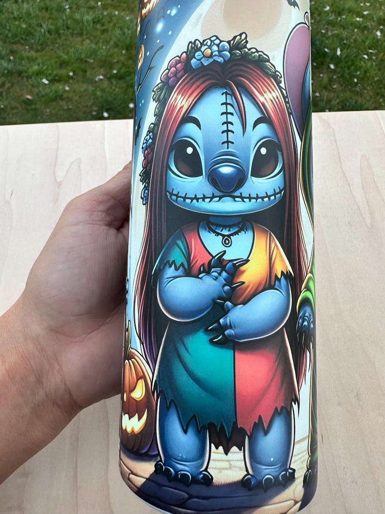 May include: A cylindrical tumbler featuring a cartoon character in a Halloween theme. The character has blue skin, long red hair, and is wearing a patchwork dress. The design includes a jack-o'-lantern and a night sky background.
